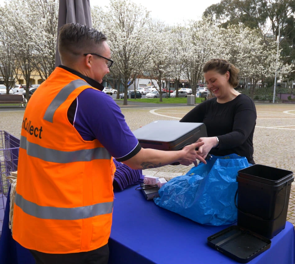 volunteer in a high vis vest receiving an old electronic device from someone recycling their tech