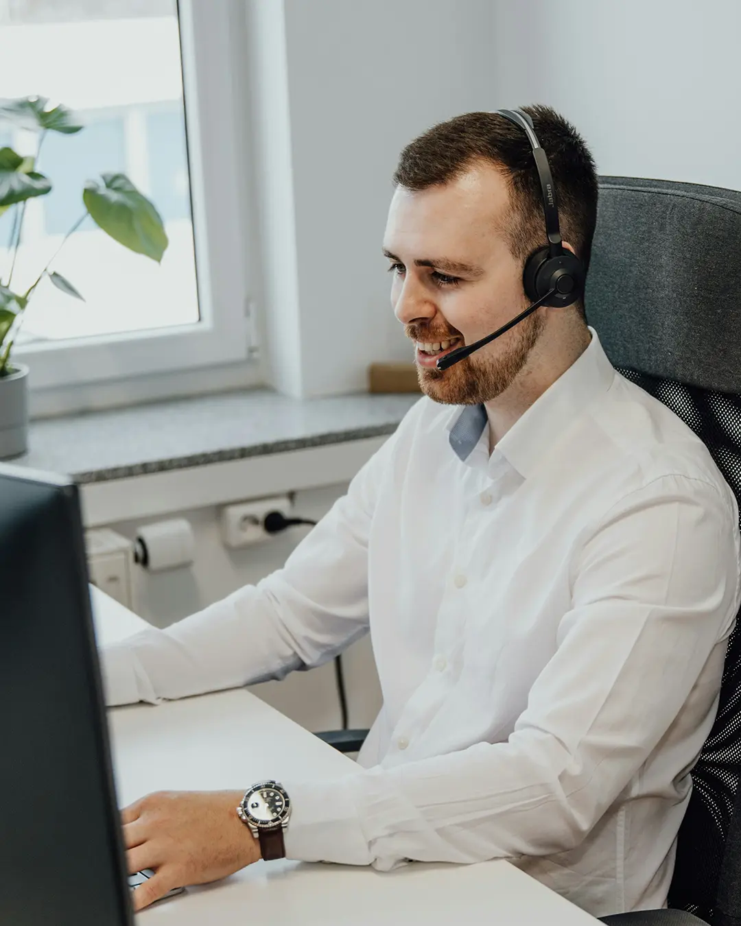 Man sitting at a desk, wearing a headset, talking to somebody on call while looking at a computer screen