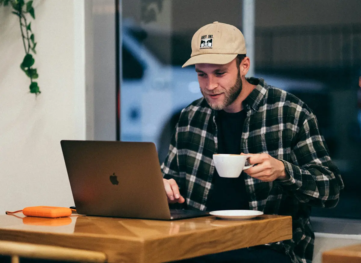 man sitting in a cafe holding a coffee cup looking at his laptop
